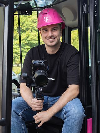 Nick Schneider (Corporate Communications Trainee) sits in the cockpit of a Magenta excavator with his camera equipment.